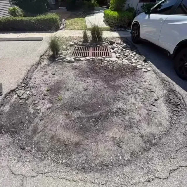 A bare, sandy curb island around a storm drain